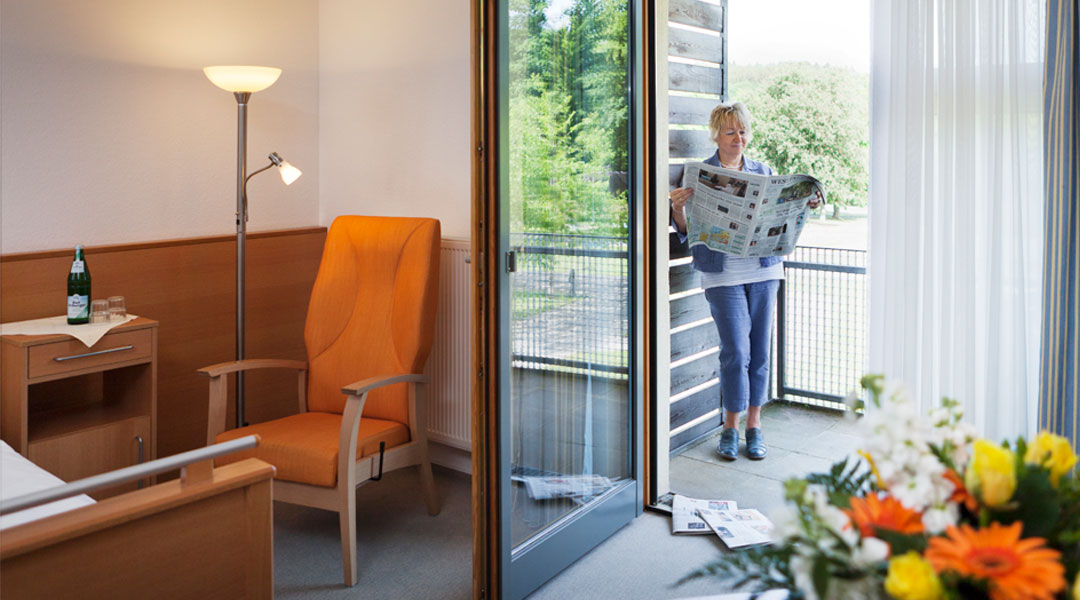 Frau liest auf dem Balkon Ihres Patientenzimmers Zeitung Park Klinik
