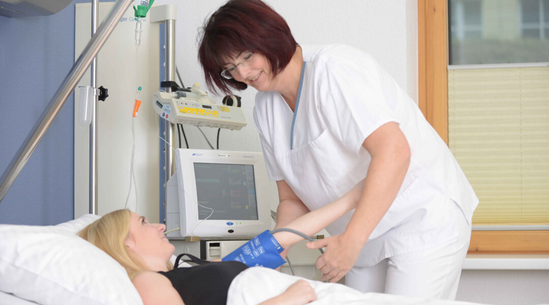 Pflegerin misst Blutdruck bei Frau im Bett in der Park Klinik