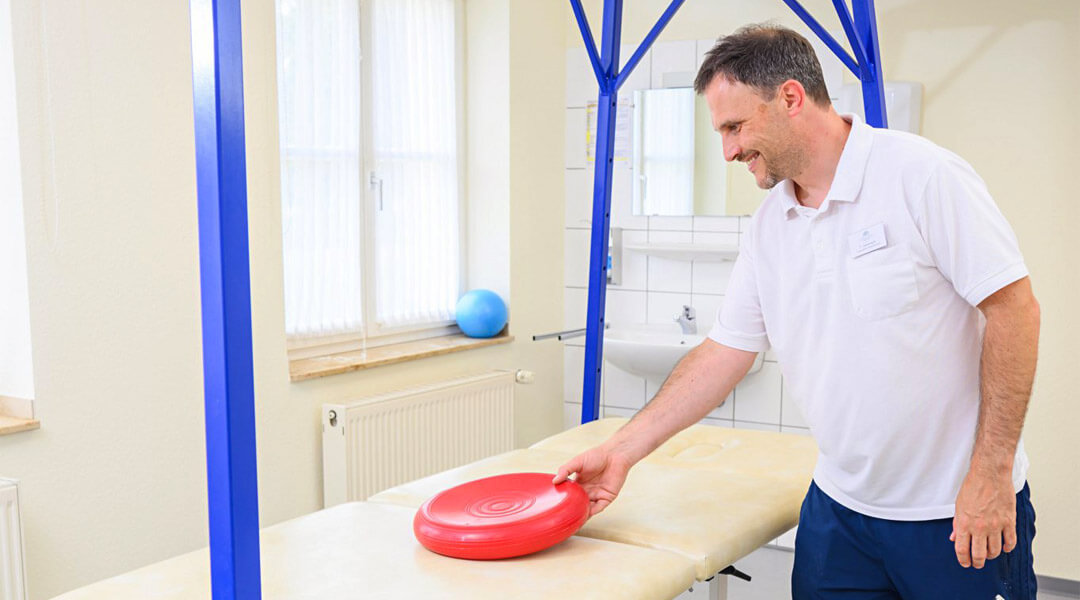 Physiotherapeut mit Sitzkissen neben Behandlungsliege